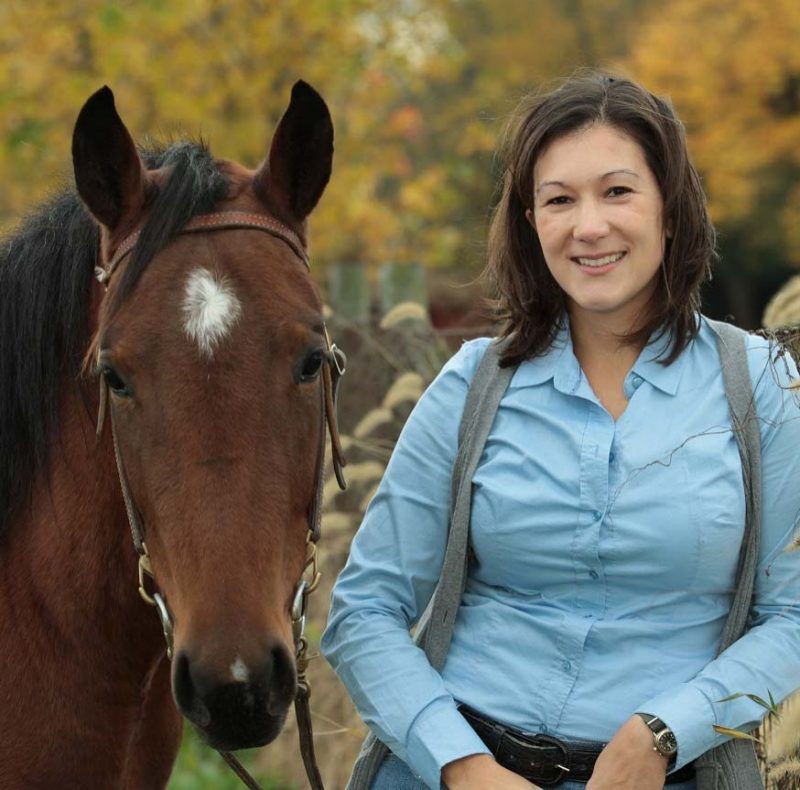 Dr. Jessica Suagee Bedore with her horse by a fence. Fall foliage in the background.